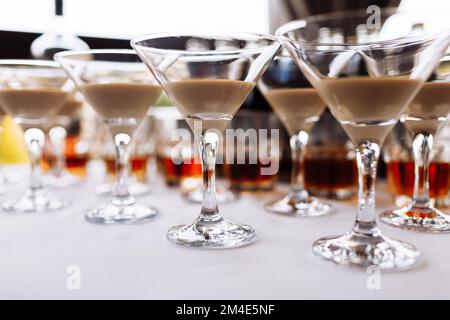 Many martini glasses with alcohol cream coffee irish cocktail, on white table background. Irish cream baileys liqueur for party. Trendy autumn winter Stock Photo