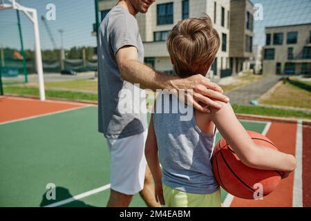 Close up of happy father and son playing basketball together and standing on court embracing Stock Photo
