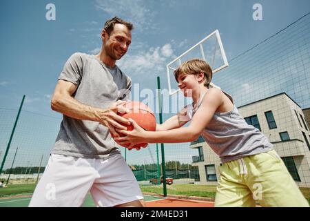 Side view portrait of father and son playing basketball together and smiling happily Stock Photo