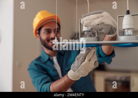 Professional electrician in uniform is installing the light bulbs into the chandelier at home Stock Photo