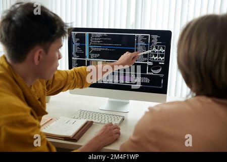 College students working on project together and discussing programming code and chart on screen Stock Photo