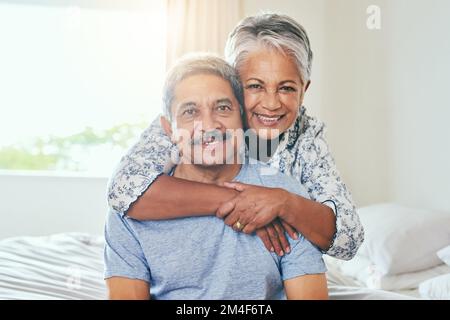 We have come a long way. Portrait of a cheerful mature couple holding each other while being seated on a bed at home during the day. Stock Photo