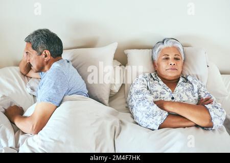What did I do wrong now. an irritated looking mature couple lying in bed facing away from each other after having an argument at home during the day. Stock Photo