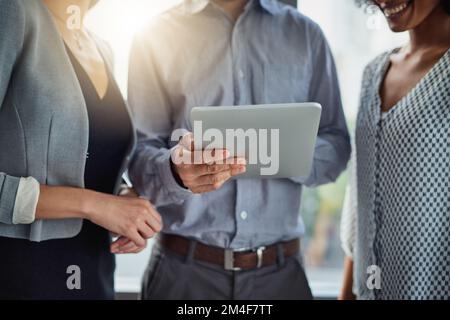 The digital team gets things done. a group of businesspeople using a digital tablet together in a modern office. Stock Photo