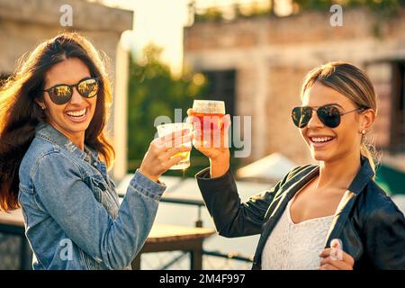 Cheers to having each other as best friends. two female best friends spending the day outside on a rooftop. Stock Photo