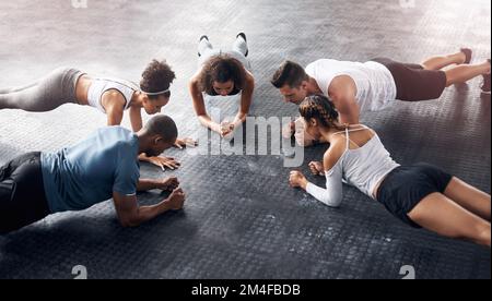 If you can plank you can do anything. a group of young people doing planks together during their workout in a gym. Stock Photo