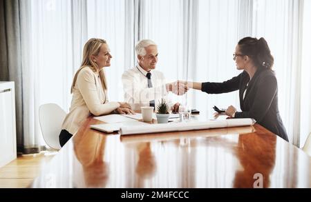 Its a pleasure doing business with you. a group of architects working together on blueprints of a house around a table while shaking hands in Stock Photo