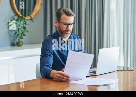 Luckily Im not at the office today. a focussed middle aged businessman sorting out documents and working from home during the day. Stock Photo