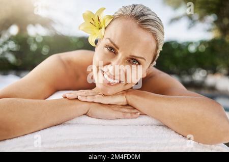 Ive been looking forward to this massage. Portrait of a cheerful middle aged woman lying on her stomach waiting to get a massage at a spa outside Stock Photo