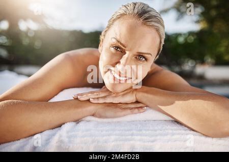 Free your mind and relax. Portrait of a cheerful middle aged woman lying on her stomach waiting to get a massage at a spa outside during the day. Stock Photo