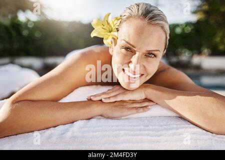 This spa is the best. Portrait of a cheerful middle aged woman lying on her stomach waiting to get a massage at a spa outside during the day. Stock Photo