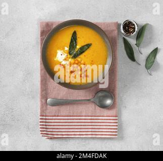 Pumpkin cream soup with sage and chikpeas and feta in a plate on a textile background, top view Stock Photo