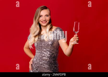 female looking at camera and holding empty clean transparent wine glass against red background Stock Photo