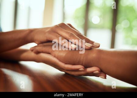 You have nothing to fear. Closeup of two unrecognizable peoples hands holding each other while resting on top of a wooden table. Stock Photo