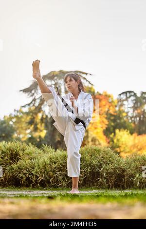 Fighter woman in kimono and black belt standing in karate position outdoors in nature. Sports and martial arts concept. Stock Photo