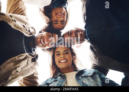 Never a dull moment with you guys. Low angle portrait of a group of young friends huddled together while looking down at the camera outside during the Stock Photo