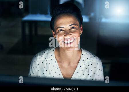 Her job makes her happy. Portrait of a cheerful young female programmer working on a computer in the office at work during the night. Stock Photo