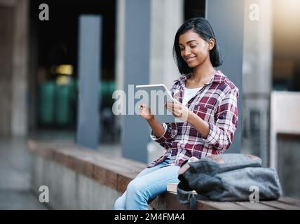 Making the most of the campus wifi. an attractive young female student using her tablet while sitting outside on campus. Stock Photo