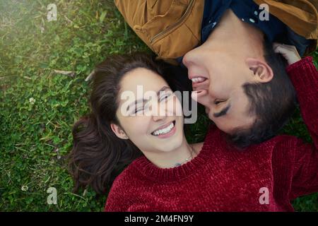 Everyone deserves someone who makes them smile. High angle shot of a happy young couple laying together on the grass. Stock Photo