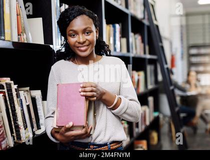 Learning new things every step of the way. Portrait of a happy young woman carrying books in a library at college. Stock Photo