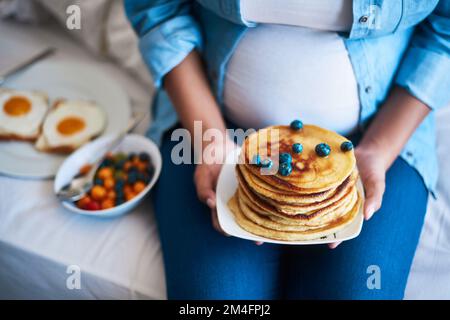 The baby ordered something sweet off the menu. a pregnant woman eating delicious pancakes at home. Stock Photo