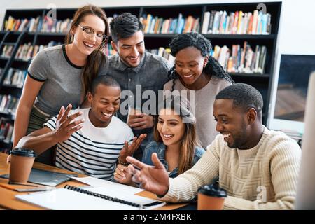 Gathered for the good of their education. a group of young students working on an assignment together in a college library. Stock Photo