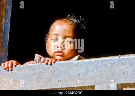 Little boy curiously looking out of the window in the small village of Gangi. Stock Photo