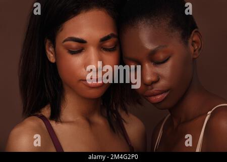 Close up of two beautiful women. Females with closed eyes head to head against a brown backdrop. Stock Photo