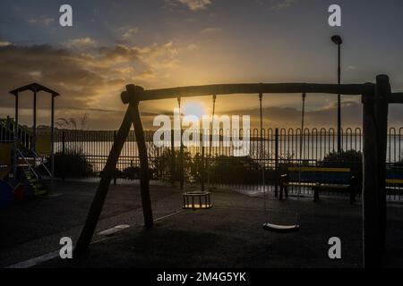 Schull, West Cork, Ireland. 21st Dec, 2022. The sun rises from behind clouds over Schull playground and moored fishing trawler 'Laetitia' in Schull Harbour on the shortest day of the year. Credit: AG News/Alamy Live News Stock Photo