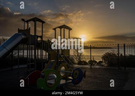 Schull, West Cork, Ireland. 21st Dec, 2022. The sun rises from behind clouds over Schull playground and moored fishing trawler 'Laetitia' in Schull Harbour on the shortest day of the year. Credit: AG News/Alamy Live News Stock Photo