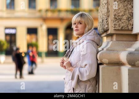 Portrait of adult alone Caucasian woman posing at column in city square. Copy space. Concept of psychology and loneliness. Stock Photo