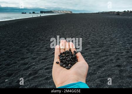 Close up woman showing handful of black pebbles on beach concept photo Stock Photo