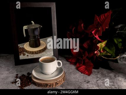 Cup of coffee on wood with a mirror where the coffee pot with red flower is reflected in a black background Stock Photo