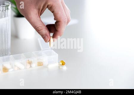 Closeup of female elderly hand taking medicine from medical pill box, sorting pills. Tablet doses for daily take with different drugs and capsules. Young woman getting her daily vitamins at home Stock Photo