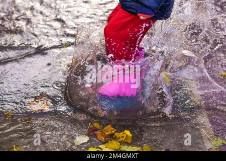 child splashing water with boots and water pants in a puddle on a rainy day Stock Photo