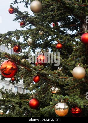 Closeup of festively decorated outdoor christmas tree with bright red and beige balls on blurred background. Stock Photo