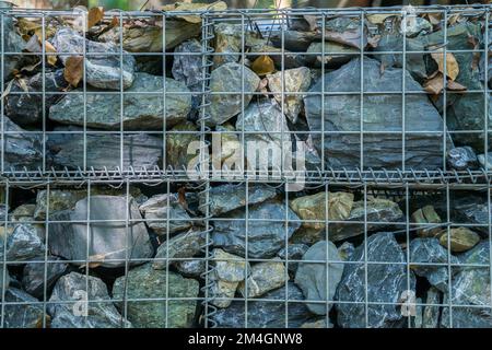 Decorative fence of bulk stone in the grid. Textured background of a stone wall with iron netting. Stone wall in wire frame. Gabion filled with limest Stock Photo