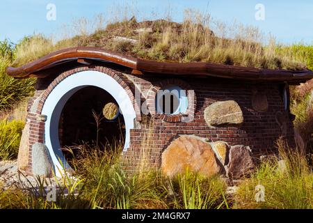 Brick cottage in the garden with a round door and grass on the roof. Stock Photo