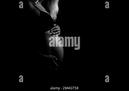 Black and white view of pregnant woman touching her belly. Pregnancy, maternity, preparation and expectation concept. Stock Photo