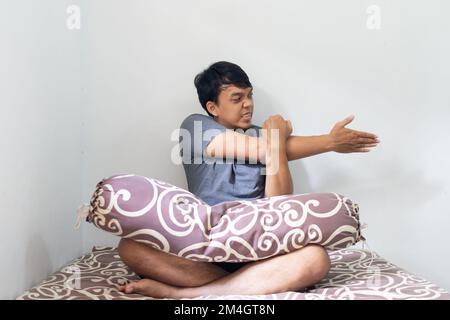 Portrait Asian Indonesian man stretching his hands in a bedroom after wake up from sleep home healthy concept isolated white background Stock Photo