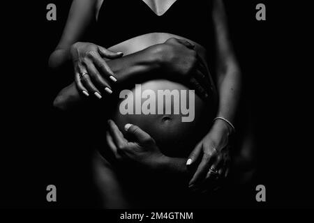 Male and female hands hug the belly of a pregnant woman. Black and white shooting. Stock Photo