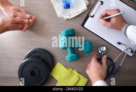 Physiotherapist doctor with patient taking notes on consultation table with medical control and sports equipment. Top view. Stock Photo