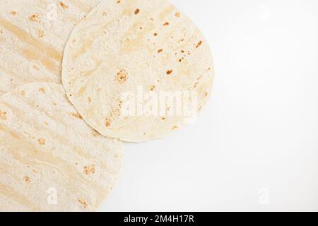 Plain wheat tortilla wraps. Spanish or Mexican circular unleavened flatbread from wheat flour. Ingredient for cooking fast food or snack. Closeup, white background, copy space Stock Photo