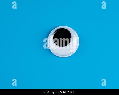 single wobbly googly eye isolated on a light blue  background with copyspace business logo Stock Photo