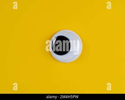 single wobbly googly eye isolated on a yellow background with copyspace business logo Stock Photo
