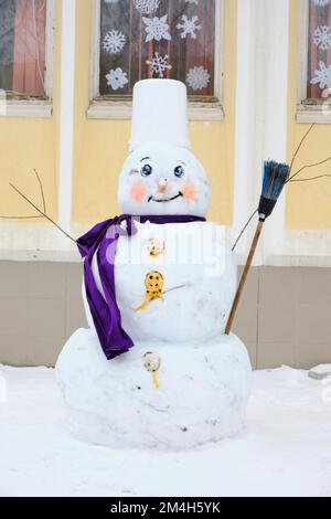 Snowman made of snow with lilac scarf and broom Stock Photo
