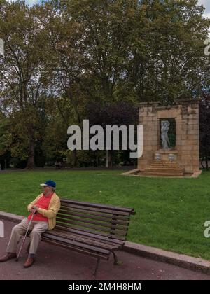 Man sentado en un banco del parque Fuente con rostros y escultura en el Jardín del Museo de Bellas Artes de Bilbao España, Europa. Stock Photo