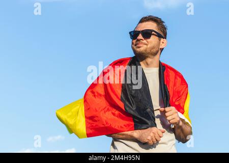 Flag of Germany on shoulders of man in sunglasses against blue sky. Stock Photo