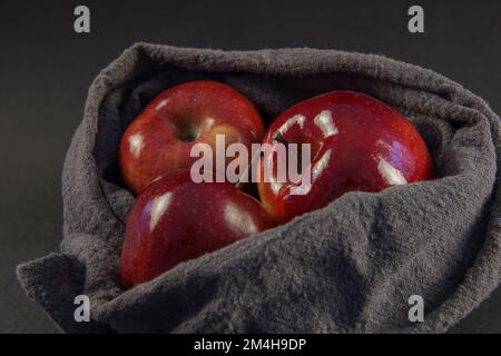 Three glosy delicious red apples in a gray basket against the dark background Stock Photo