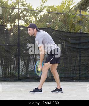 Young bearded man wearing cap plays tennis outdoors. Stock Photo